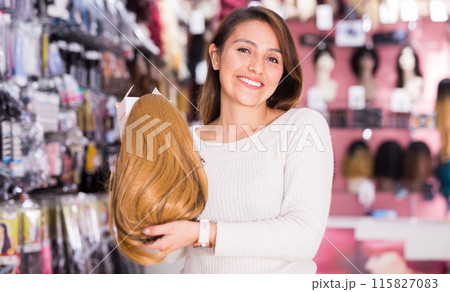 Cheerful young Latina selecting natural hair wigs in store Cheerful young Latina selecting natural hair wigs in store 115827083