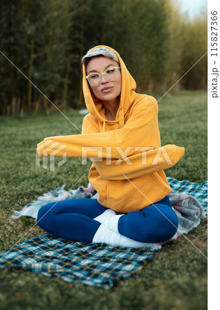 cute girl with glasses in an orange hoodie is sitting in a park in nature expressing kind emotions cute girl with glasses in an orange hoodie is sitting in a park in nature expressing kind emotions 115827366