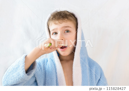 small child, boy in a blue terry robe with a toothbrush on white. A child brushes his teeth. Healthcare and dental care small child, boy in a blue terry robe with a toothbrush on white. A child brushes his teeth. Healthcare and dental care 115828427