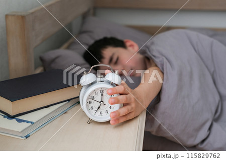 Sleepy boy reaches for the alarm clock. Morning of the schoolboy Sleepy boy reaches for the alarm clock. Morning of the schoolboy 115829762