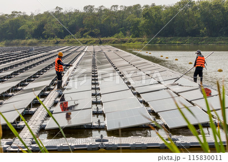Worker Cleaning floating solar panels or solar cell Platform system on the lake with brush and water 115830011
