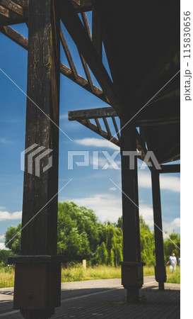 The pillars of a wooden gazebo overlooking the park and the lake The pillars of a wooden gazebo overlooking the park and the lake 115830656