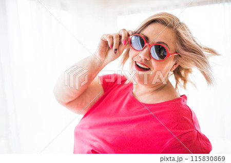 Portrait of beautiful young overweight woman at home, with sunglasses. 115830869