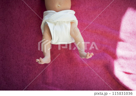 Portrait of legs of little newborn baby lying on bed, wearing diaper. 115831036