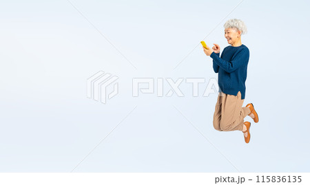 スマホを見ながらジャンプするシニア女性の全身写真 115836135