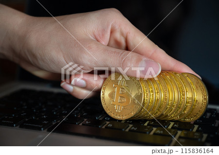 Close up of human hand put some pieces of golden Bitcoin token on laptop. Bitcoin is one of the popular cryptocurrency, a virtual currency or a digital currency. 115836164