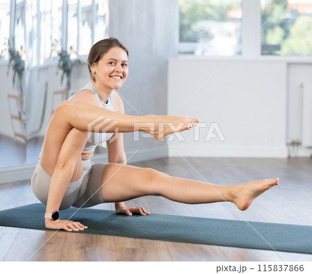 Smiling yogi teacher doing scale yoga pose in gym. Young woman practicing advanced yoga on mat in yoga studio 115837866