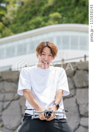 晴れの屋外でドローン撮影を楽しむ日本人男性｜ドローンイメージ 115838143