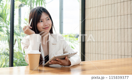 An attractive, thoughtful Asian businesswoman is working remotely from a cafe, using her tablet. An attractive, thoughtful Asian businesswoman is working remotely from a cafe, using her tablet. 115839377
