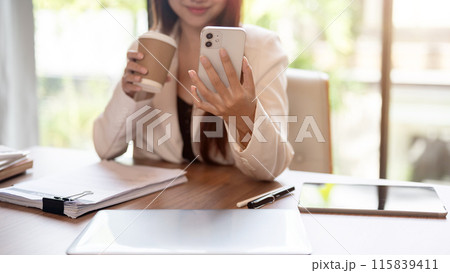 A cropped image of a positive, beautiful Asian businesswoman is using her smartphone at her desk. 115839411
