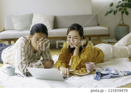リビングの床に寝そべってソートパソコンを見る若いカップル 115839470
