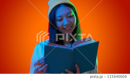 Enjoying reading. Woman book. Cheerful focused female holding textbook exciting education rest happy pastimes green blue neon light isolated on red gradient empty space background. Enjoying reading. Woman book. Cheerful focused female holding textbook exciting education rest happy pastimes green blue neon light isolated on red gradient empty space background. 115840009