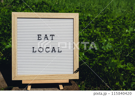 Letter board with text EAT LOCAL on background of garden bed with green herb parsley. Organic farming, produce local vegetables concept. Supporting local farmers 115840420
