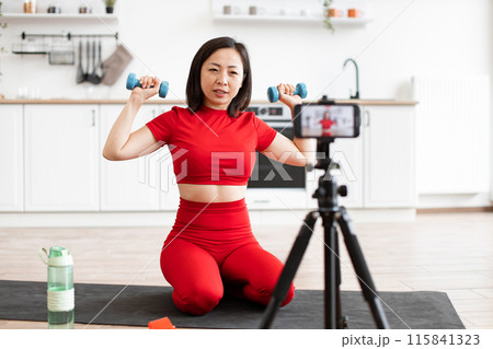 Woman exercising with dumbbells during home workout session Woman exercising with dumbbells during home workout session 115841323