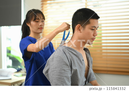 Rehabilitologist or physiotherapist applying Kinesio tape on patient neck during the medical treatment at clinic 115841332