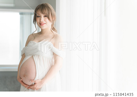 家のカーテンの前でマタニティフォトの撮影をする妊婦のアジア人女性 115841435