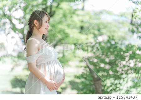 新緑の木漏れ日の中マタニティフォトの撮影をするアジア人妊婦の女性 新緑の木漏れ日の中マタニティフォトの撮影をするアジア人妊婦の女性 115841437