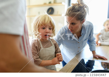 Young boy burn his finger while helping in kitchen. Mother soothing him. 115843447