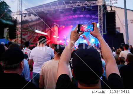 Person standing in front of stage, recording live music concert on smartphone Person standing in front of stage, recording live music concert on smartphone 115845411