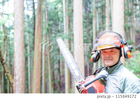 手入れをした森をバックにチェンソーを携えて微笑みを浮かべているフォレストワーカー 115849172