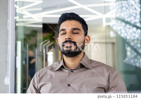 A calm man with his eyes closed is meditating in a contemporary office environment. This serene moment captures the essence of stress relief and mindfulness practice in a work setting A calm man with his eyes closed is meditating in a contemporary office environment. This serene moment captures the essence of stress relief and mindfulness practice in a work setting 115851184