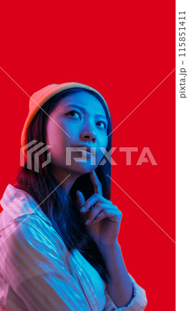 Skeptic face. Idea contemplation. Blue pink neon light pensive girl considering solution isolated on red copy space background. 115851411