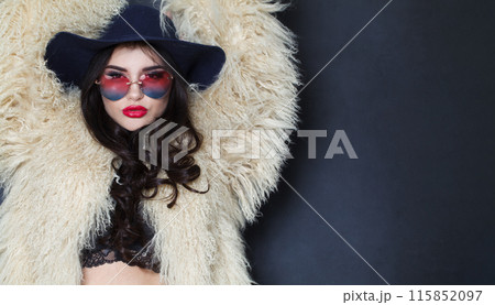 Glamorous young adult woman fashion model with bright make-up and long wavy hair wearing blue hat  115852097