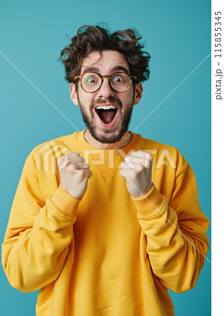 Excited Young Man in Yellow Sweater Expressing Joy with Fists Raised 115855345
