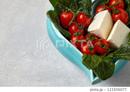 Cherry tomatoes, brine cheese and spinach in a blue decorative bowl on a gray stone table 115856077