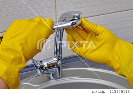 Kitchen faucet repair. A worker in yellow rubber gloves uses an adjustable wrench to unscrew the aerator 115856118