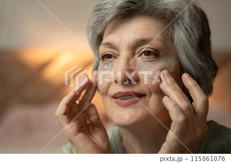In the evening, an elderly woman puts eye patches on her face. Close-up and shows the expression of a woman's face when she applies patches In the evening, an elderly woman puts eye patches on her face. Close-up and shows the expression of a woman's face when she applies patches 115861076