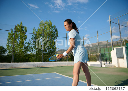 Woman in her 40s playing tennis on an outdoor court under a clear sky 115862187