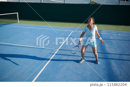 Woman in her 40s playing tennis on court, focused and ready for serve 115862204