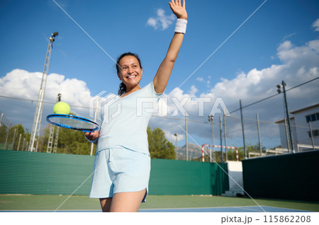 Healthy middle-aged woman playing tennis on an outdoor court and smiling Healthy middle-aged woman playing tennis on an outdoor court and smiling 115862208
