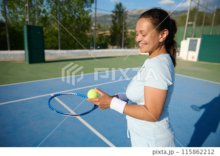 Middle-aged woman playing tennis on outdoor court with smile and tennis racket 115862212