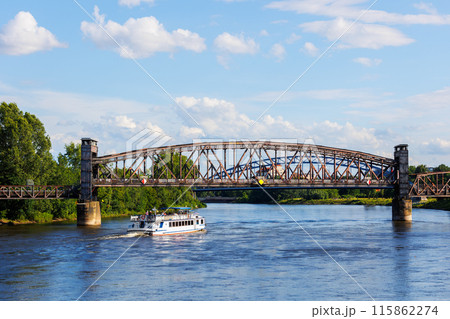 Tourist boat cruises under old historic iron bridge on Elbe River in Magdeburg, Germany with blue sky clouds background landscape. Saxony-Anhalt center cityscape sightseeing water trip Tourist boat cruises under old historic iron bridge on Elbe River in Magdeburg, Germany with blue sky clouds background landscape. Saxony-Anhalt center cityscape sightseeing water trip 115862274