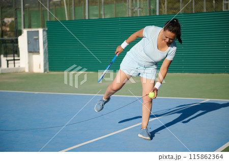 Middle-aged woman playing tennis on outdoor court, practicing forehand swing 115862364