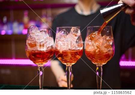 Bartender pours pink cocktail into martini glass with flair Bartender pours pink cocktail into martini glass with flair 115863562