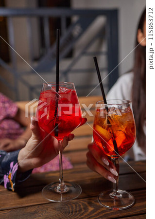 Two friends lifting cocktails in a lively bar scene, expressing joy and celebration 115863712