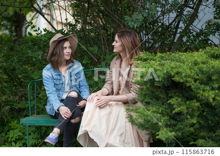 Lovely friends talking and sitting on a park bench outdoors Lovely friends talking and sitting on a park bench outdoors 115863716
