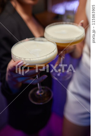 A woman holds a cocktail in her hand, with her fingers wrapped around the glass 115863905