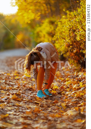 elegant woman in fitness clothes in park tying shoelaces 115864332