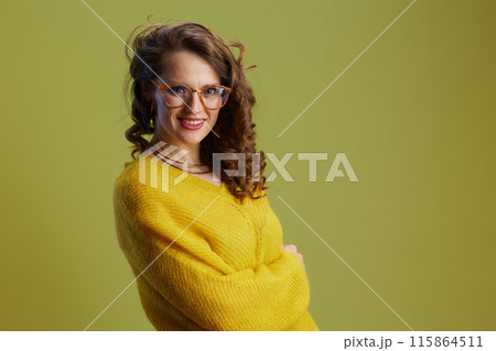 smiling trendy woman in sweater and glasses isolated on green 115864511
