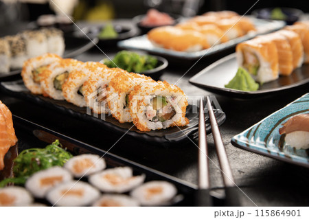 Top view of traditional japanese cuisine . Sushi rolls set with salmon , tuna fish and vegetable served on black stone table . Asian food on black stone slate with chopsticks . Top view of traditional japanese cuisine . Sushi rolls set with salmon , tuna fish and vegetable served on black stone table . Asian food on black stone slate with chopsticks . 115864901