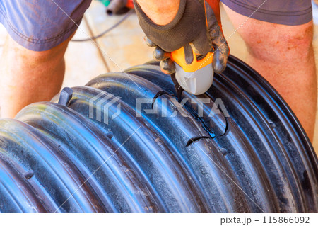 Drilling hole in black plastic polypropylene sanitary pipe in order to connect it to another pipe 115866092