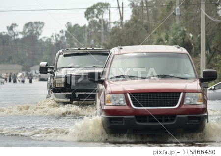 Hurricane flooded street with moving cars and surrounded with water houses in Florida residential area. Consequences of natural disaster 115866480