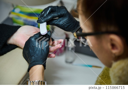 Manicure process at a beauty salon with nail technician filing nails 115866715