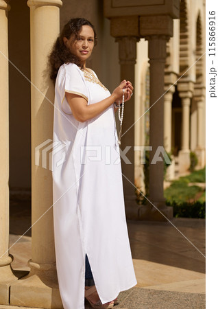 Woman in traditional white dress holding prayer beads outside a historic building Woman in traditional white dress holding prayer beads outside a historic building 115866916