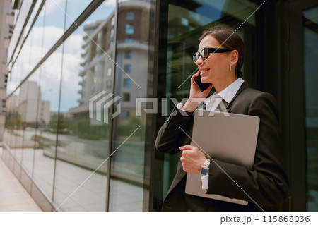 A confident businesswoman is multitasking, talking on the phone and holding a laptop A confident businesswoman is multitasking, talking on the phone and holding a laptop 115868036