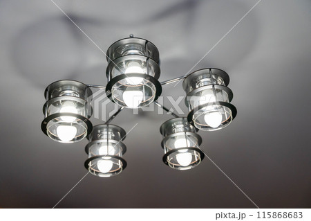 A modern black metal chandelier with five glass shades hangs from a ceiling A modern black metal chandelier with five glass shades hangs from a ceiling 115868683